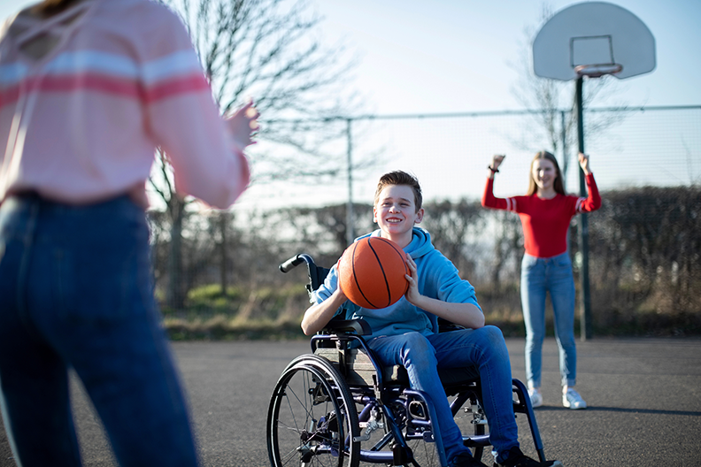 3 jeunes jouent au basketball; celui au centre est en fauteuil roulant