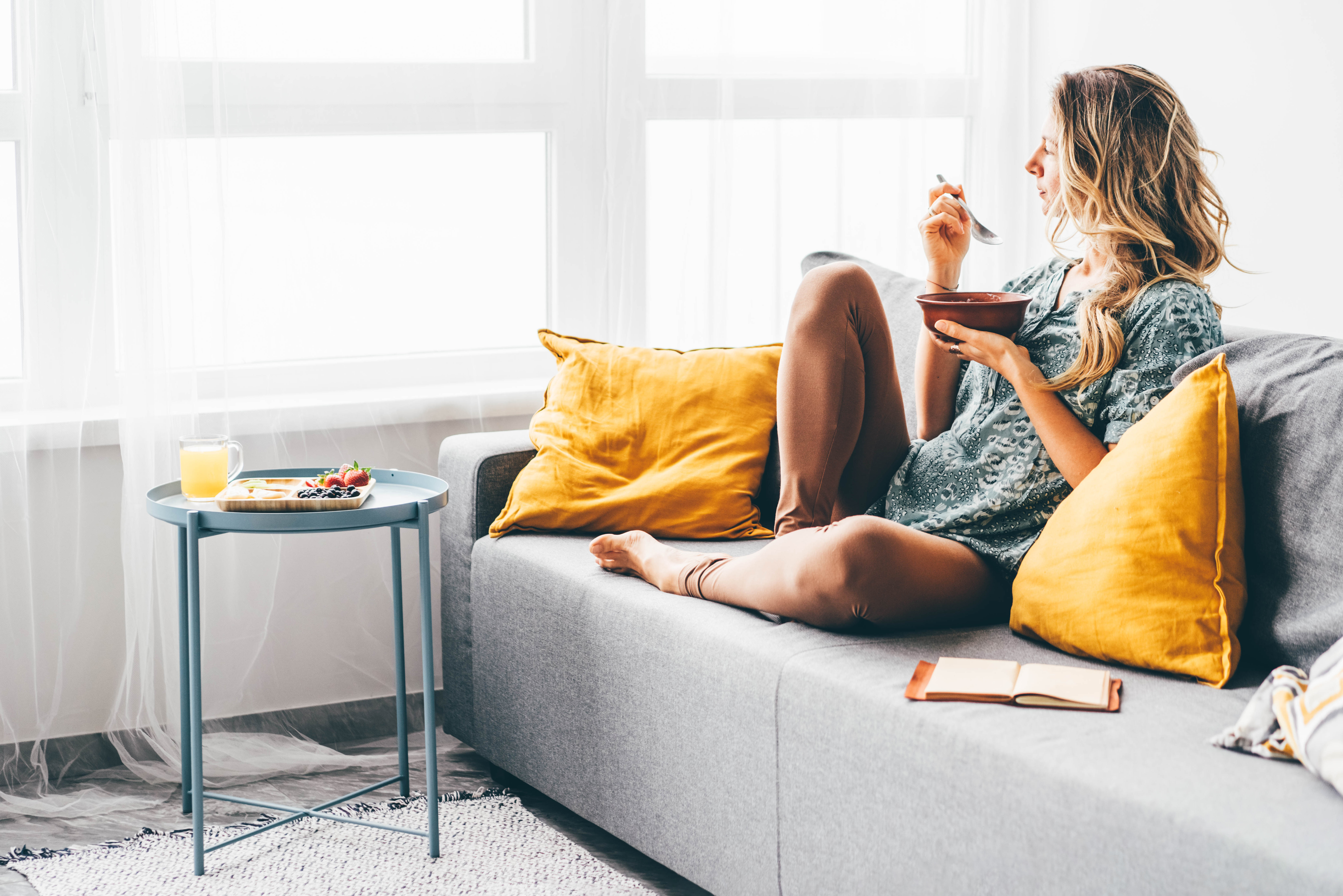 Femme assise, détendue sur un sofa, mange dans un bol, regarde par le fenêtre